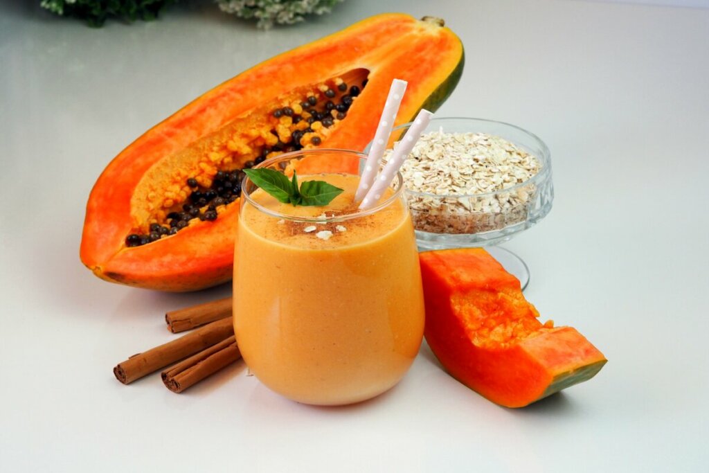 Copo de vidro com vitamina de mamão decorada com flocos de aveia e folhas de hortelã