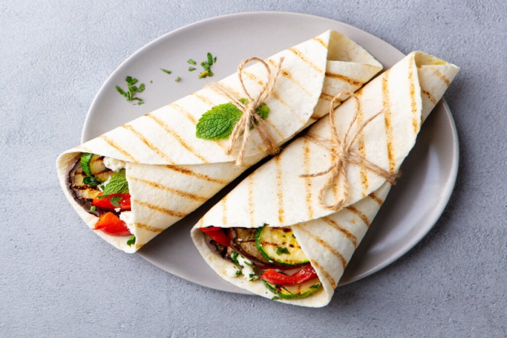 Dois wraps de legumes grelhados com queijo feta, amarrados com barbante e servidos em prato cinza