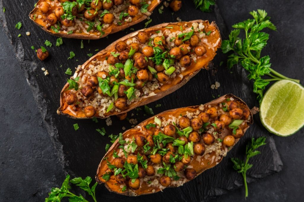 Batata-doce laranja recheada com quinoa e grão-de-bico servida em cima de mesa de pedra