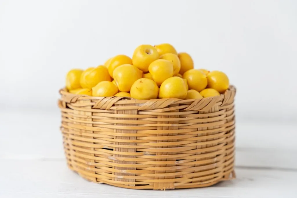 Cesto de vime com diversas frutas murici em cima de bancada de pedra branca em fundo branco