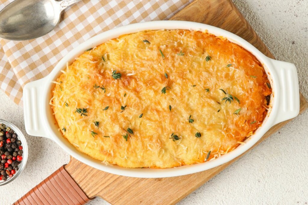 Travessa branca com arroz de forno coberto com queijo em cima de tábua 
