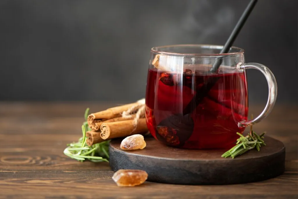 Xícara de vidro com chá vermelho ao lado de canelas em pau e sobre um pires