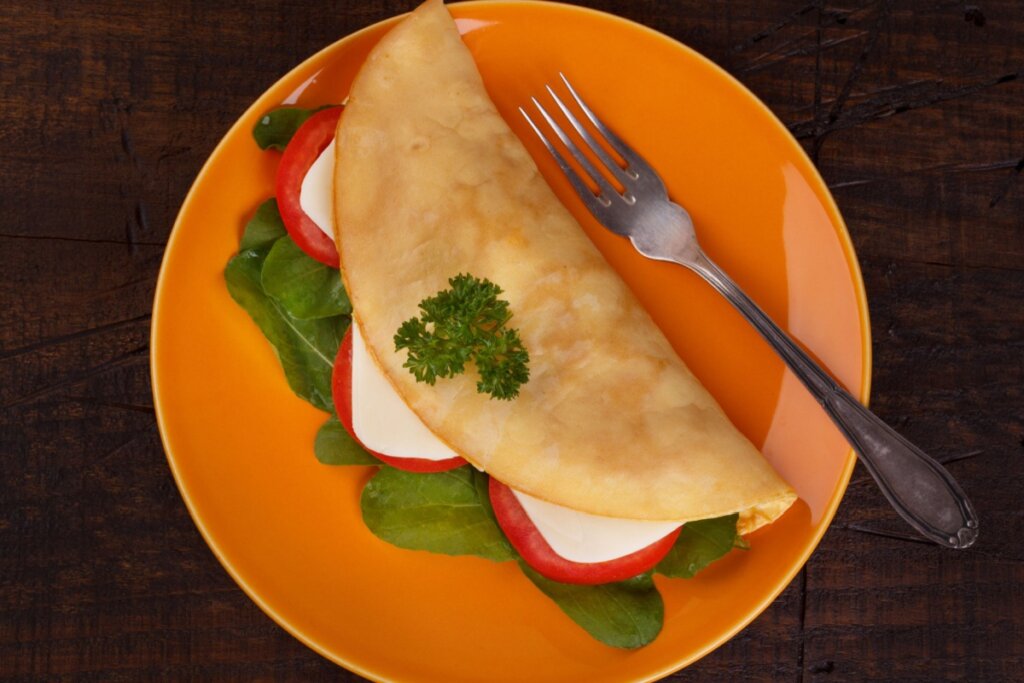 Prato laranja com crepioca com queijo branco, tomate e espinafre