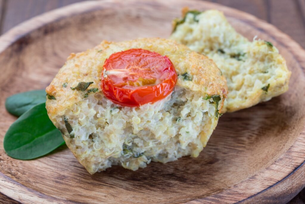 Muffin de quinoa com um tomate-cereja em cima, sobre um prato marrom, cortado ao meio