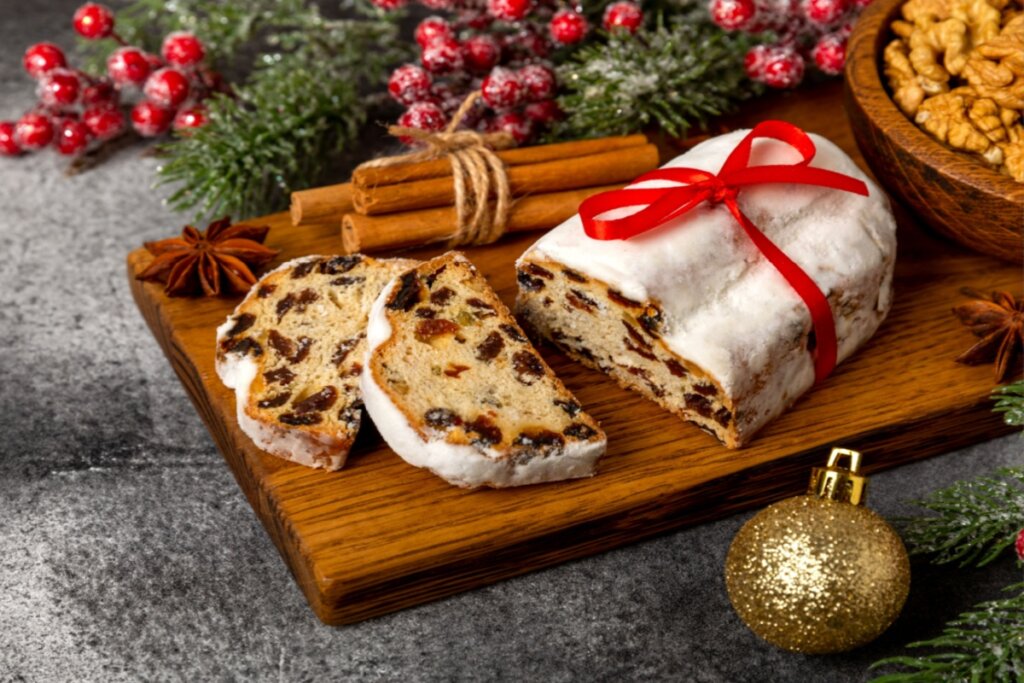 pão natalino com frutas e cobertura de açúcar em cima de tábua com decoração de natal ao fundo