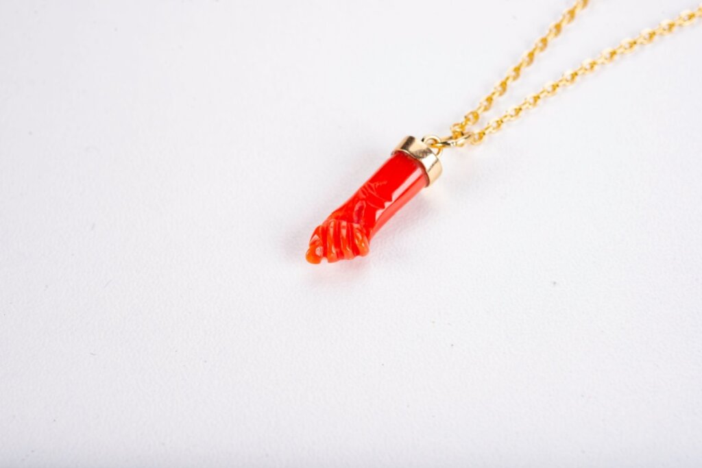 Colar dourado com figa vermelha sobre uma superfície branca 