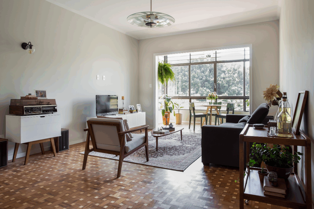 Sala de estar com móveis antigos, um sofá escuro e cadeira com estofado branco e parede de vidro ao fundo