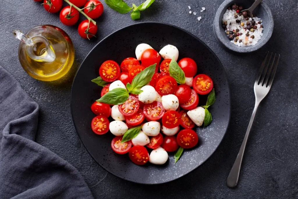 Prato preto com salada com tomates-cereja, muçarela de búfala e folhas de manjericão 
