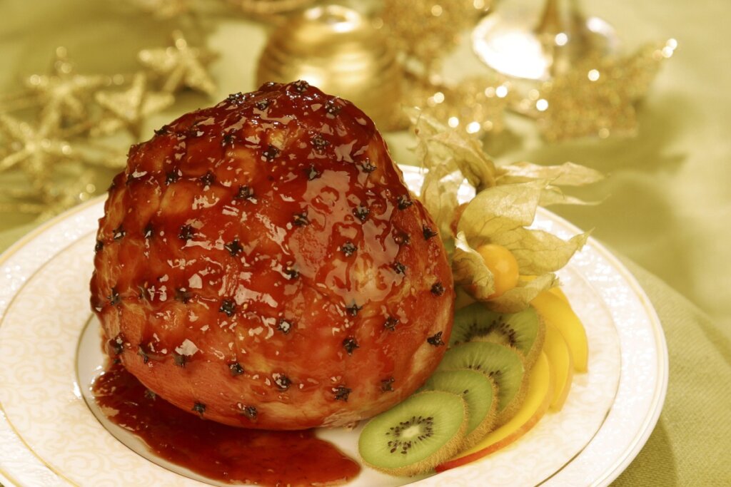 Tender com calda de manga e kiwi servido em prato branco decorado com kiwi, manga e physalis