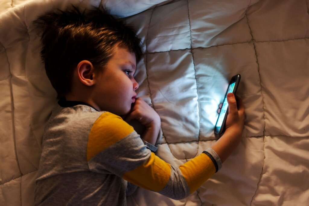 Menino deitado de lado e mexendo em um celular