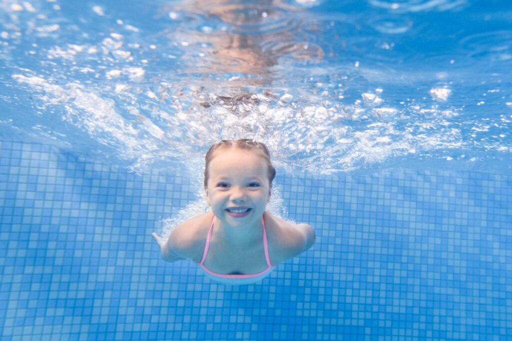 Criança nadando em piscina, submersa na água, com azulejos visíveis ao fundo
