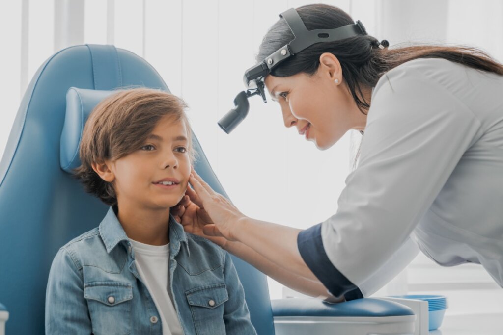 Médica examinando o ouvido de um menino sentado em uma poltrona azul 