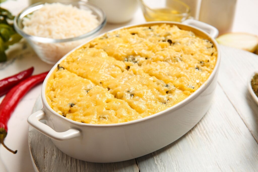 Refratário branco com arroz de forno com frango cremoso em cima de uma mesa branca