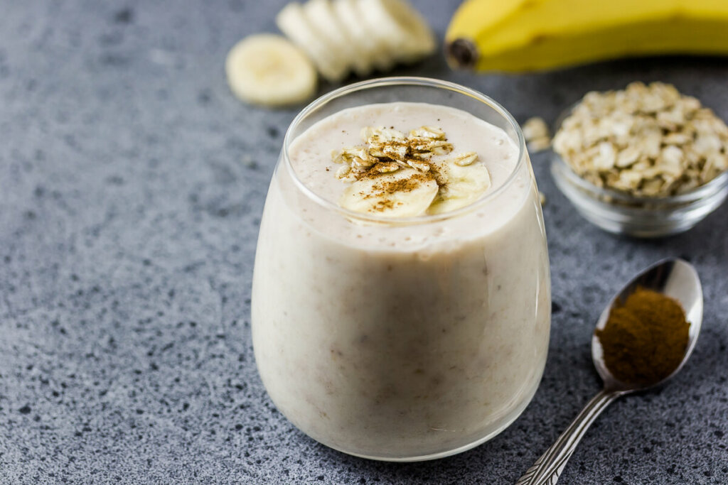 Copo de vidro com vitamina de banana decorada com rodelas de banana e canela em pó