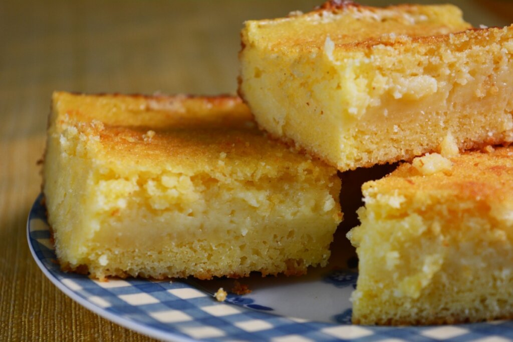 Três pedaços de bolo de fubá cremoso em cima de um prato branco e azul