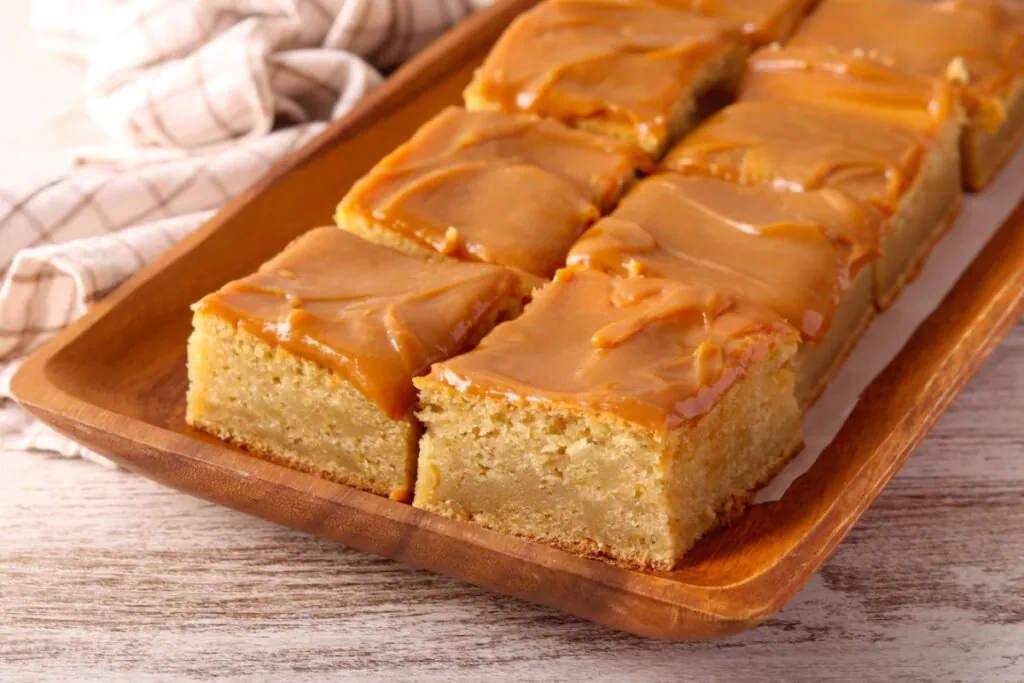 Pedaços de bolo de amendoim com cobertura cremosa em uma travessa marrom