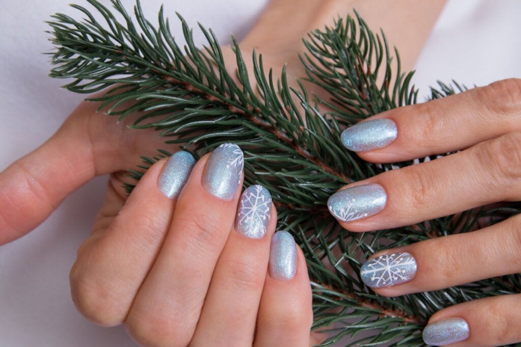 Unhas azuis com desenhos de flocos de neve. mãos segurando folhas verdes