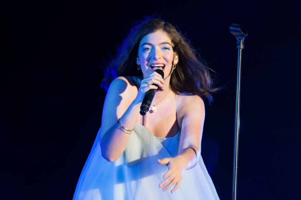 Mulher com cabelo preto, usando vestido branco cantando em palco 