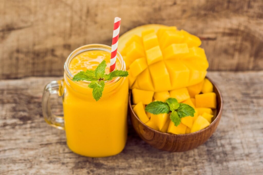 copo de vidro com vitamina amarela e pote com manga em cubos ao lado