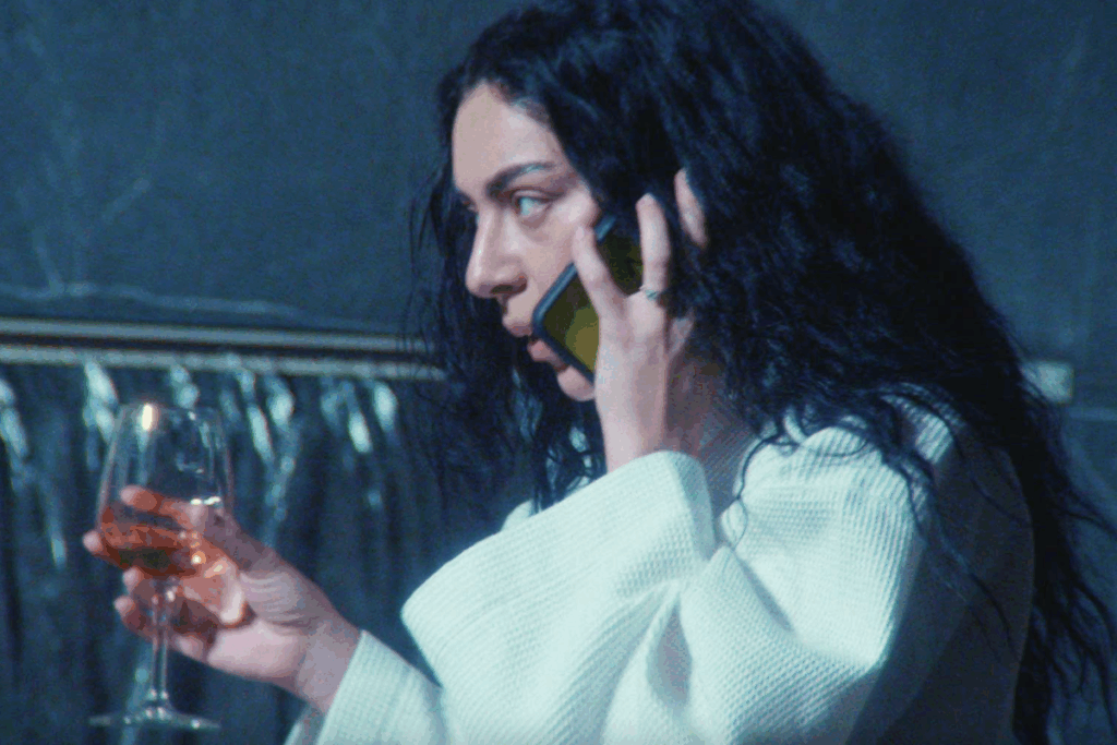 Mulher de cabelos escuros segurando uma taça de vinho rosé e falando ao telefone em ambiente com iluminação azulada