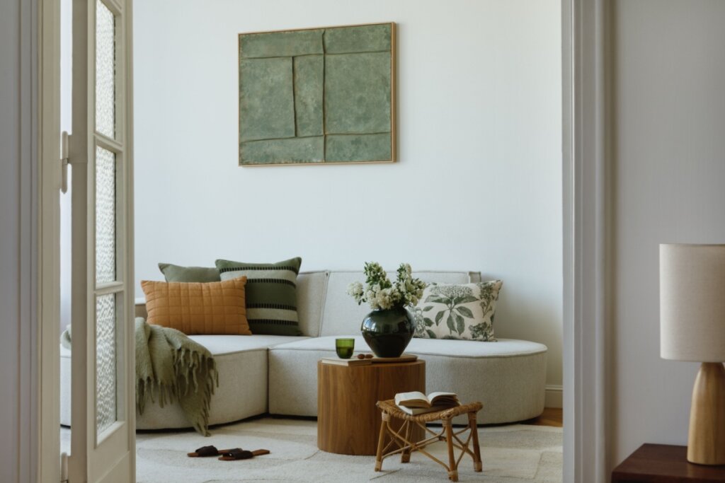 Sala de estar com sofá claro, almofadas em tons de verde e decoração natural com mesa de centro e flores