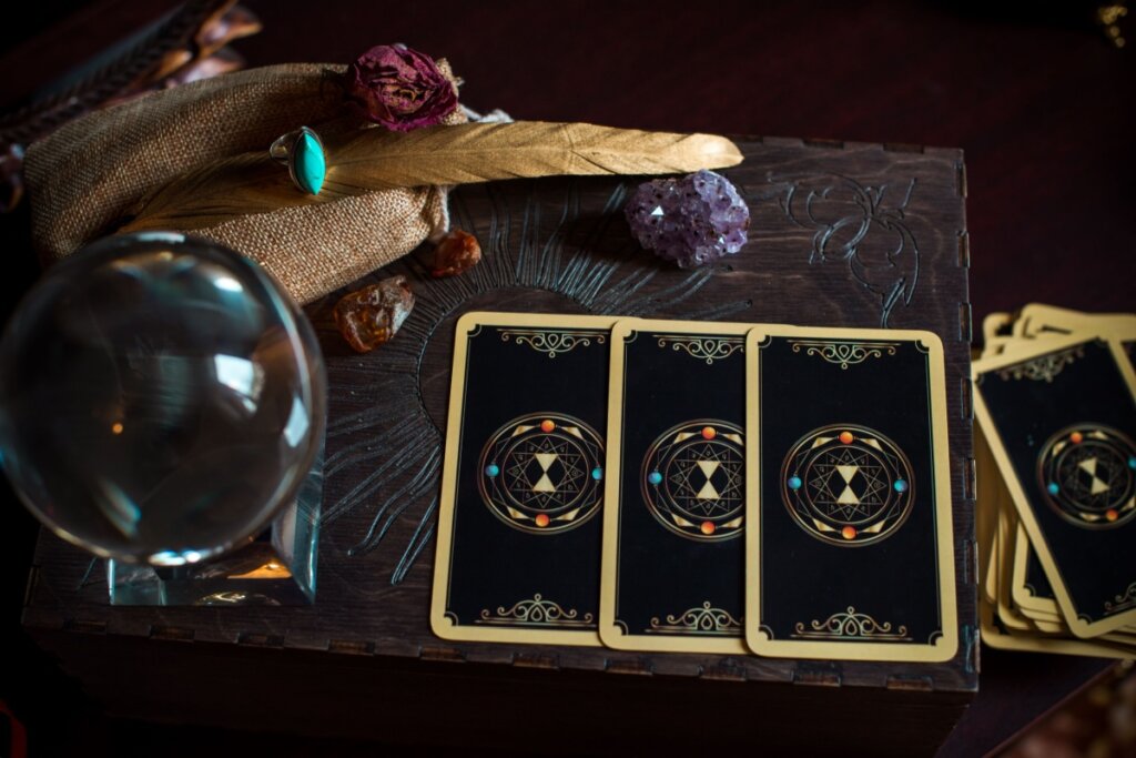 Imagem de cartas de tarot ao lado de pedras, um anel e uma bola de cristal