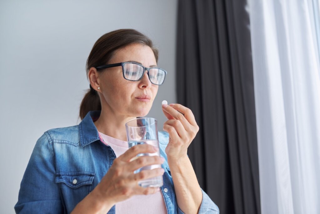 Mulher na faixa dos 40 anos tomando comprimido de reposição hormonal