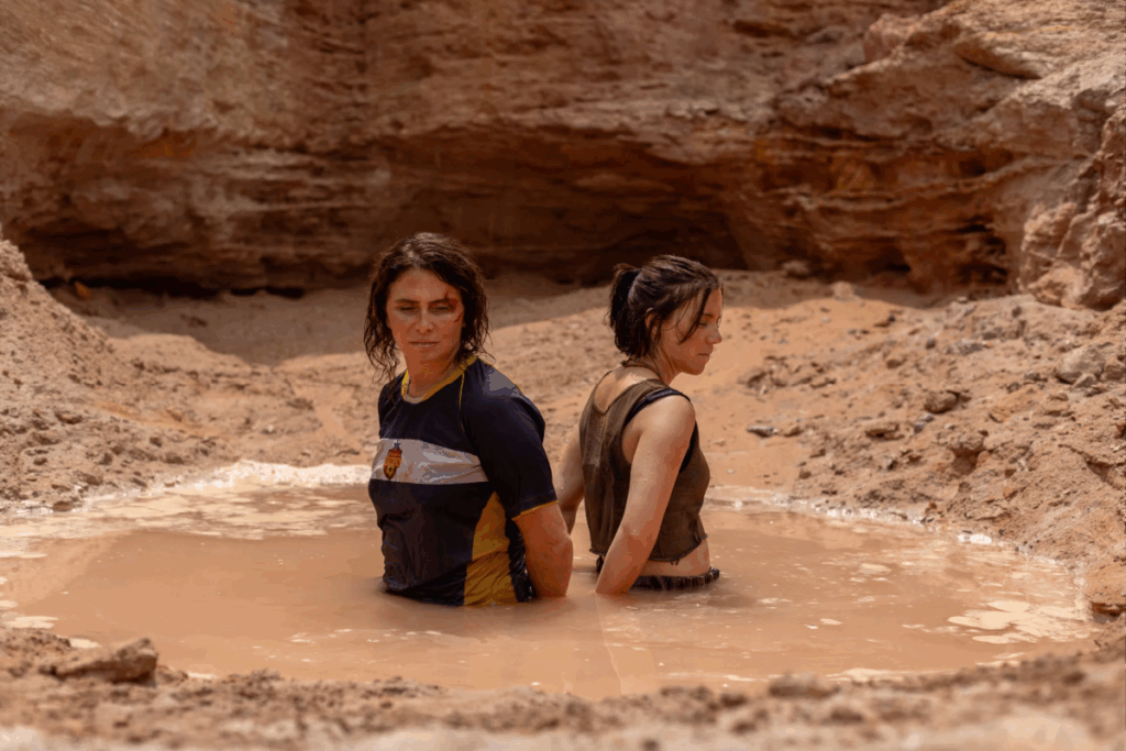 Duas mulheres presas em uma poça de lama no meio de um cenário rochoso e árido