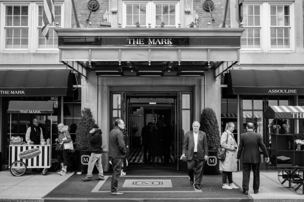 Foto em preto e branco com a fachada do Hotel The Mark enquanto pessoas andam na rua 