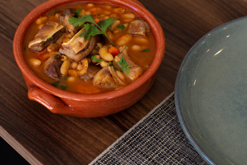 Feijoada branca com carnes em panela de barro ao lado de prato cinza
