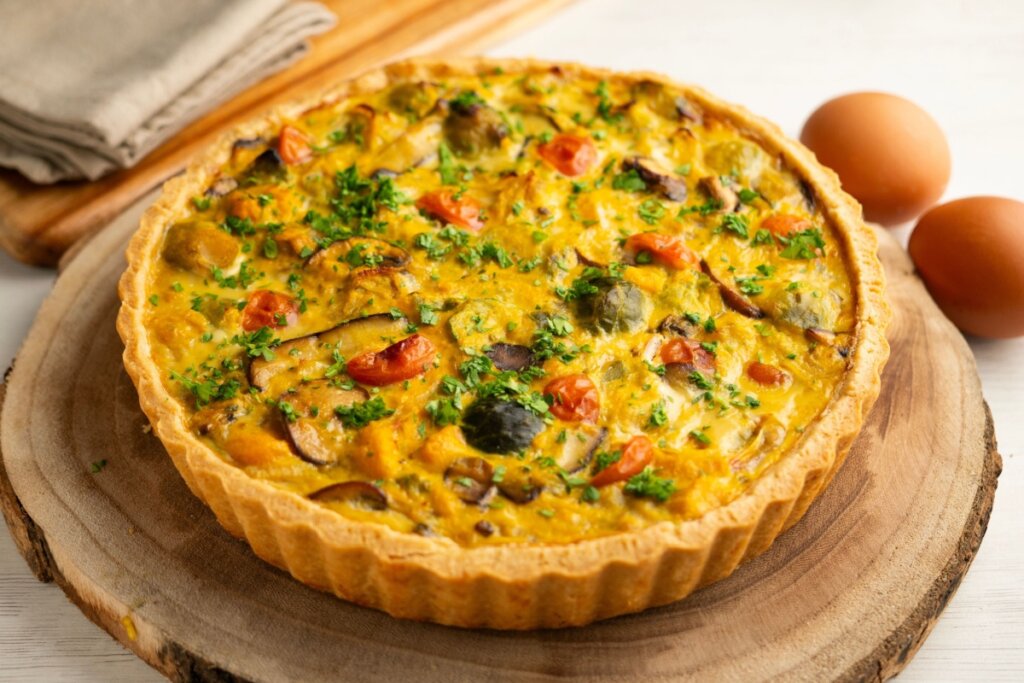 Quiche de cogumelo com legumes servido em tábua de madeira em cima de mesa de madeira 