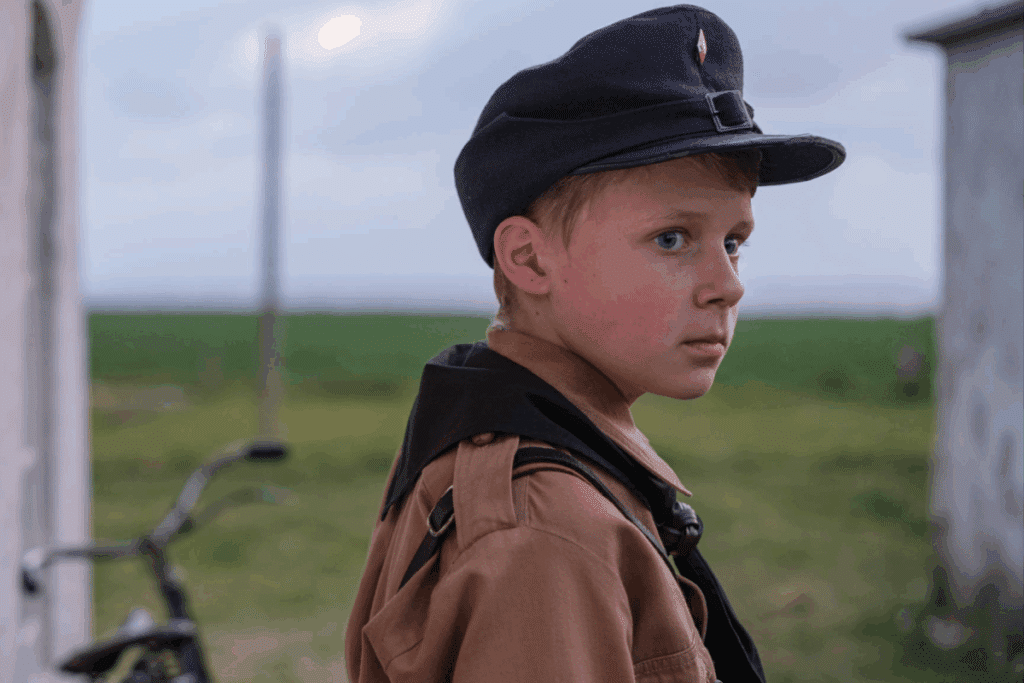 Menino usando uniforme e boné de época observando o horizonte em uma área rural