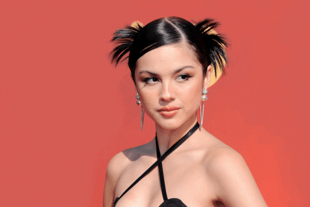 Cantora Olivia Rodrigo com cabelo no estilo Y2K, usando um vestido preto de alcinhas e posando para a foto
