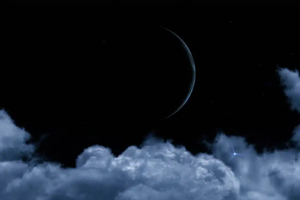 Imagem do céu noturno escuro exibindo uma fina borda prateada da Lua à direita. Na metade inferior, grandes nuvens volumosas de tom azul-acinzentado formam uma base, com uma estrela azulada bastante brilhante reluzindo entre elas à direita.