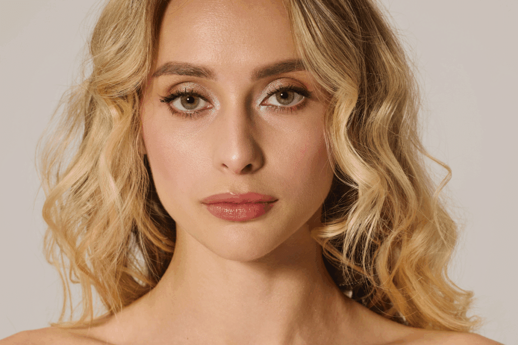 Mulher com cabelo loiro-mel ondulado no estilo Y2K Honey, olhos claros e maquiagem em tons neutros.